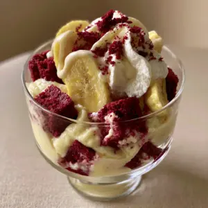 Close up of layered Red Velvet Banana Pudding in a glass showing cake cubes and fresh banana slices.