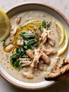 A velvety ivory broth Mediterranean White Chicken Chili garnished with a golden olive oil swirl and cracked black pepper.