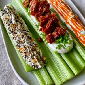 Macro top-down view of vibrant green celery stalks filled with whipped cream cheese and gourmet toppings. (Stuffed Celery recipe)